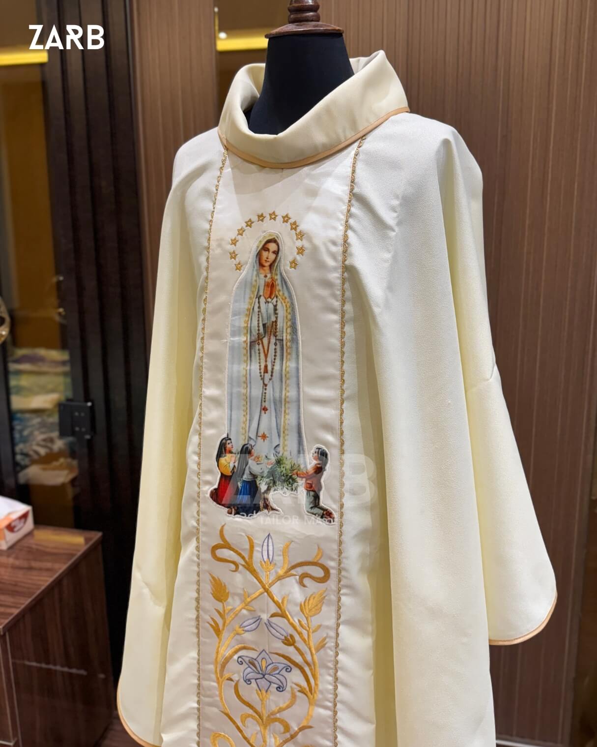 Ivory religious robe with embroidered design on a mannequin against a wooden background