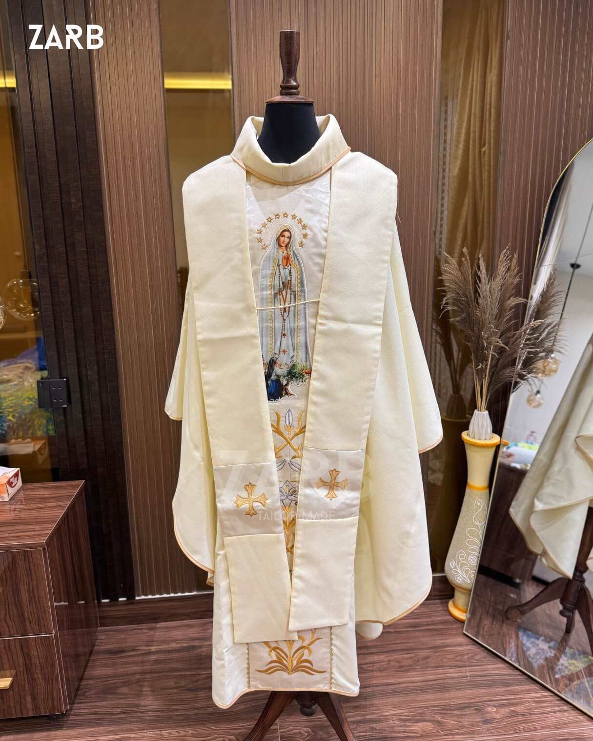 Ivory religious vestment with embroidered design on a mannequin against a wooden wall.