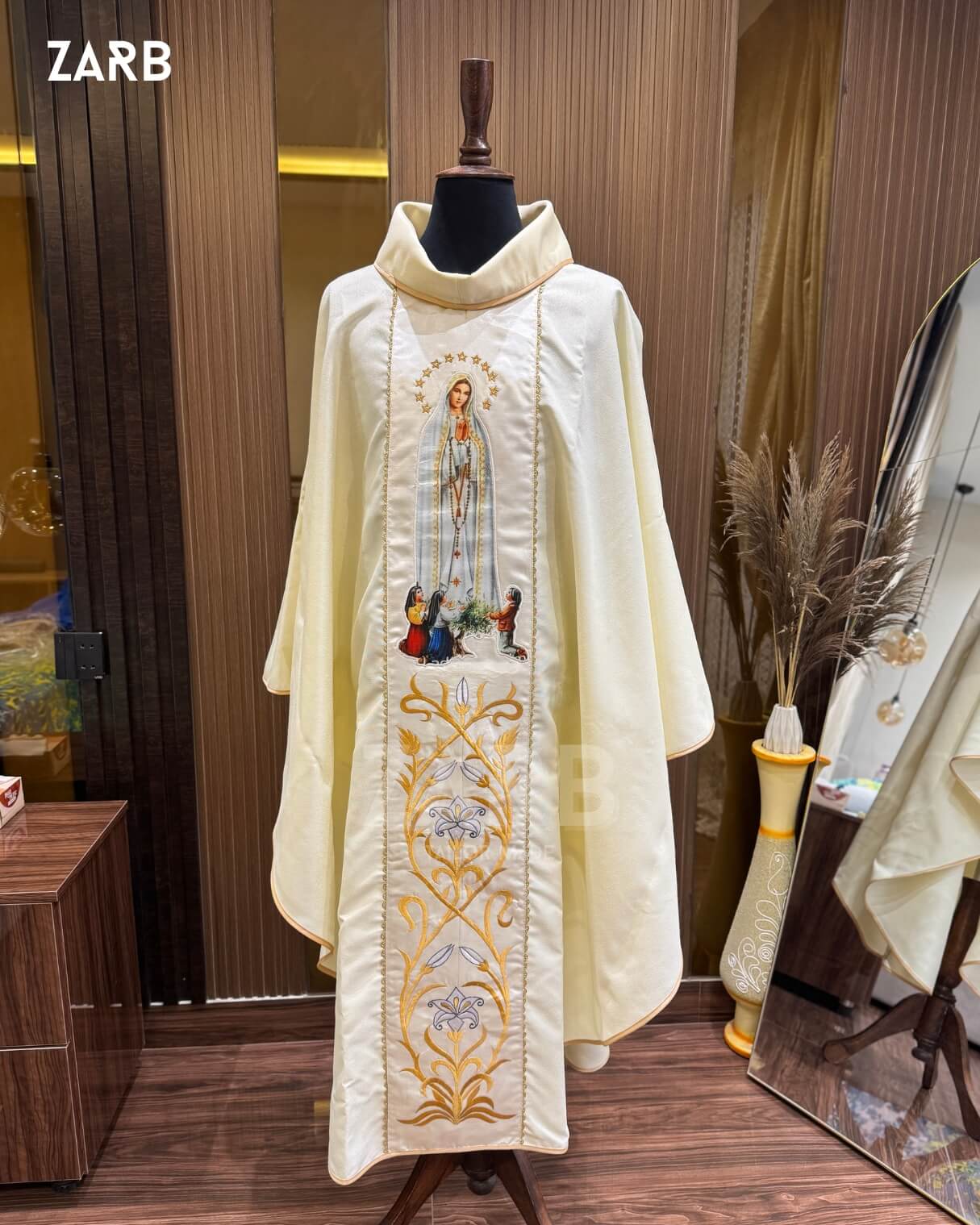 Ivory liturgical vestment with embroidery on a mannequin against a wooden wall.